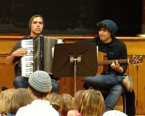 One young man playing an accordian and one playing a guitar with a music stand in front of them
