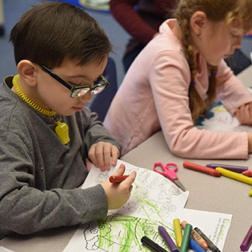 A young boy with special needs and a young girl sitting at a table coloring