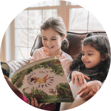 Two young girls smiling reading a J Library book together