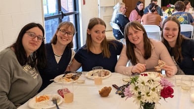 A group of young women sitting around a table, smiling and looking at the camera.