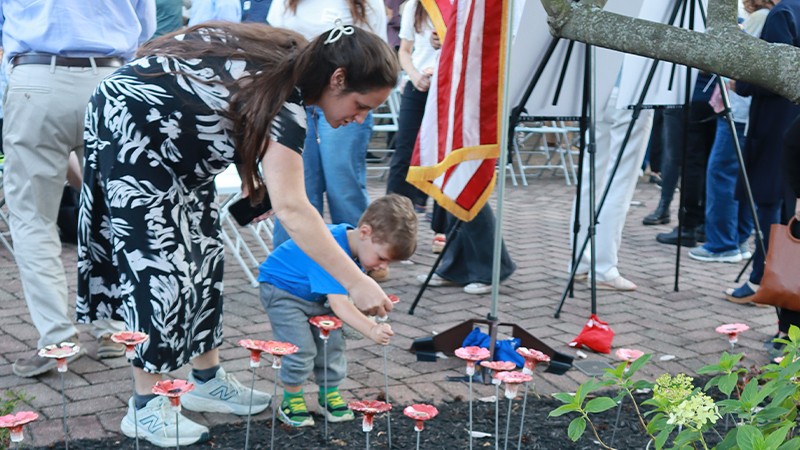 A woman and her son plant a ceramic flower in a garden as part of an October 7th remembrance ceremony
