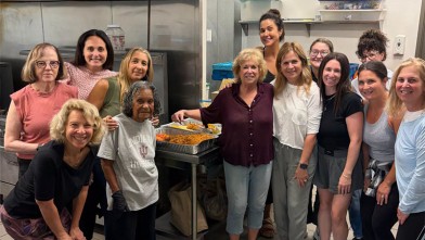 a group of women stand together smiling in a kitchen after cooking and serving a meal