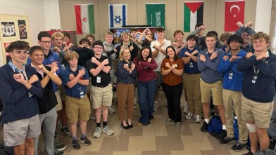 a room full of high school boys and several young women with their arms crossed in an "X"