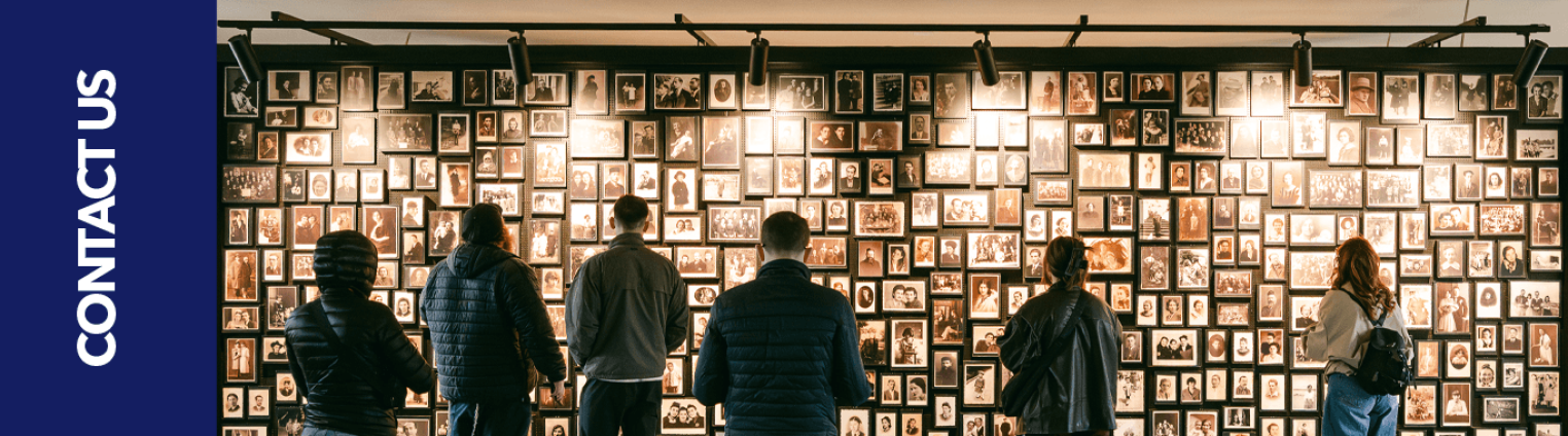Four people stand facing a wall filled with framed photographs. The bottom of the image features the text "CONTACT US".