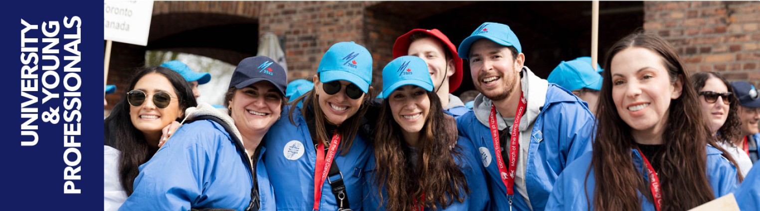 A group of six young adults wearing blue jackets and hats smiles together, with a sign the text "University & Young Professionals."