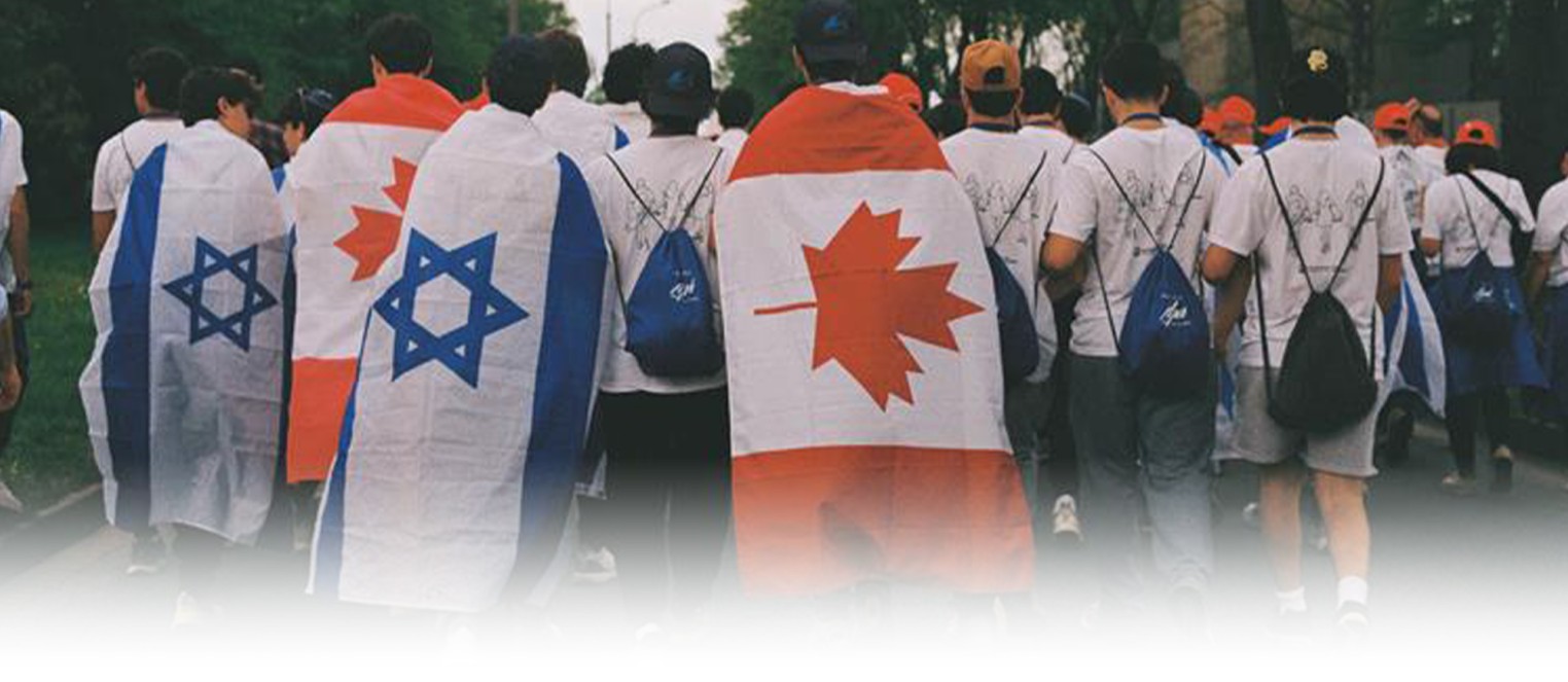 A group of people walking together, some wrapped in Israeli flags and others in Canadian flags, with backpacks on.