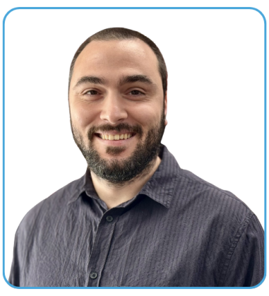 A man with a beard and short hair smiling, wearing a dark collared shirt, against a plain black background.