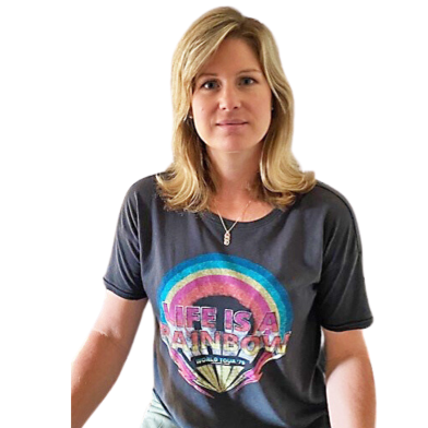 A woman with blonde hair wearing a black t-shirt featuring a colorful rainbow design and the text "LIFE IS A RAINBOW" stands against a plain background.