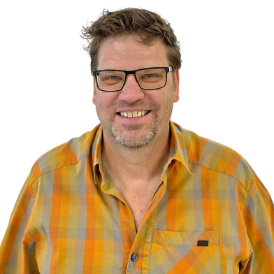 A man with short, wavy hair and glasses smiles at the camera, wearing an orange and gray plaid shirt against a white background.