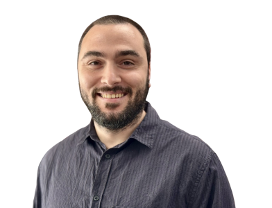A man with a beard and short hair smiles while wearing a dark button-up shirt, set against a plain white background.