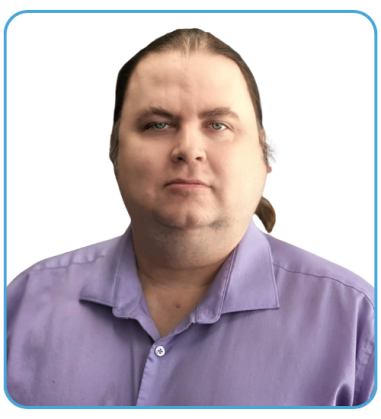 A man with long hair tied back, wearing a light purple shirt, is looking directly at the camera against a black background.