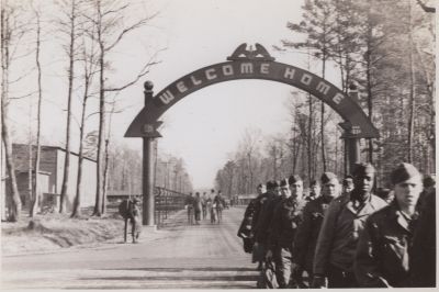 Black and white photo of soldiers walking under a large archway that reads 