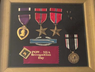 A framed display of military medals including a Purple Heart, two silver stars, and a POW-MIA Recognition Day ribbon with text.