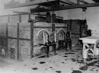 Black and white image of brick ovens with arched openings, arranged in a row, in a dimly lit room with a table in the foreground.